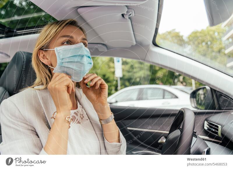 Porträt einer Frau im Auto beim Anlegen einer Schutzmaske Rückspiegel KFZ Verkehrsmittel Automobil Autos PKW PKWs Wagen zufrieden Muße auf Achse in Bewegung