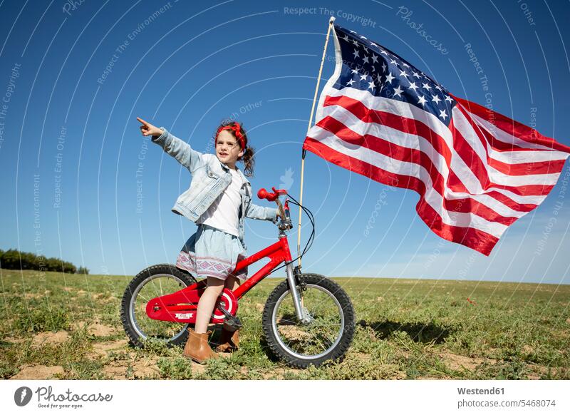 Mädchen mit Fahrrad und amerikanischer Flagge auf Feld in abgelegener Landschaft abgeschieden Felder Landschaften weiblich Fahnen Flaggen Bikes Fahrräder Räder