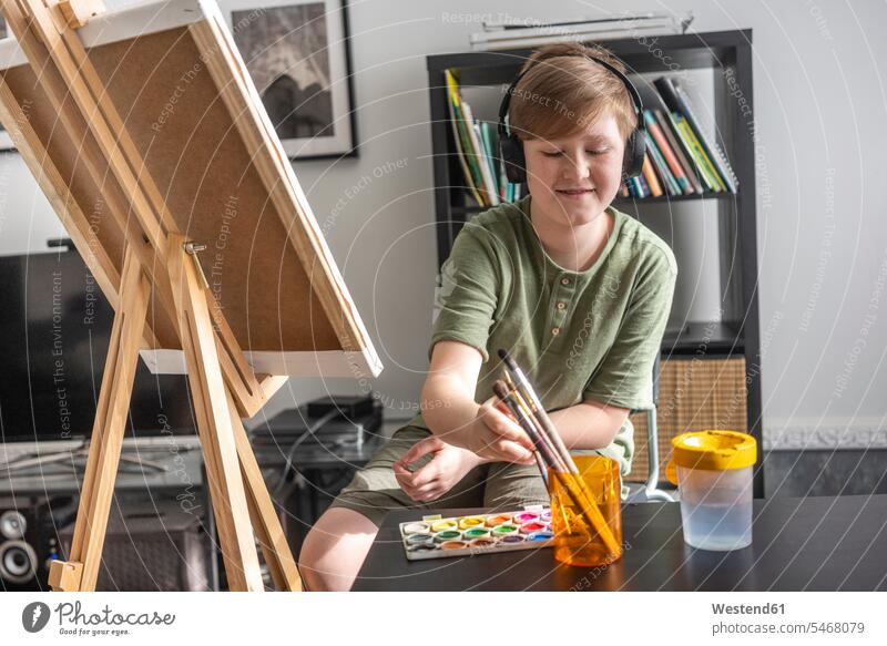 Junge malt an der Staffelei und hört Musik Kopfhoerer hoeren sitzend sitzt freuen Glück glücklich sein glücklichsein zufrieden daheim zu Hause Muße Kreativ Raum