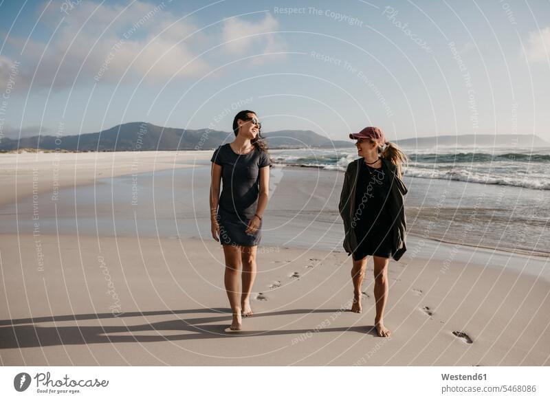 Südafrika, Western Cape, Noordhoek Beach, zwei junge Frauen schlendern am Strand spazierengehen Spaziergang machen spazieren gehen weiblich Meeresufer gehend
