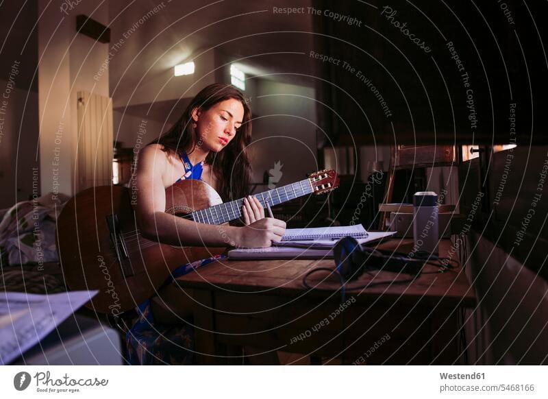 Junge Frau schreibt in Buch, während sie zu Hause Gitarre übt Farbaufnahme Farbe Farbfoto Farbphoto Zuhause Häusliches Leben Das Leben zuhause Wohnen daheim