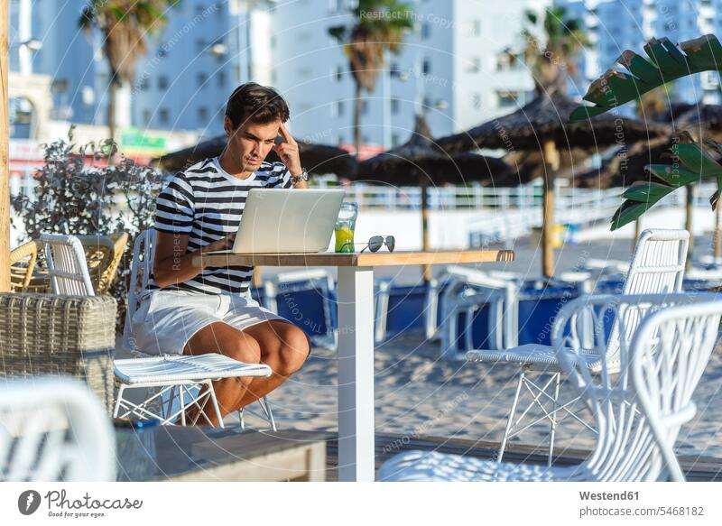 Mann mit Laptop sitzt auf der Terrasse einer Strandbar sitzen sitzend Notebook Laptops Notebooks Terrassen Männer männlich Beach Straende Strände Beaches Bar