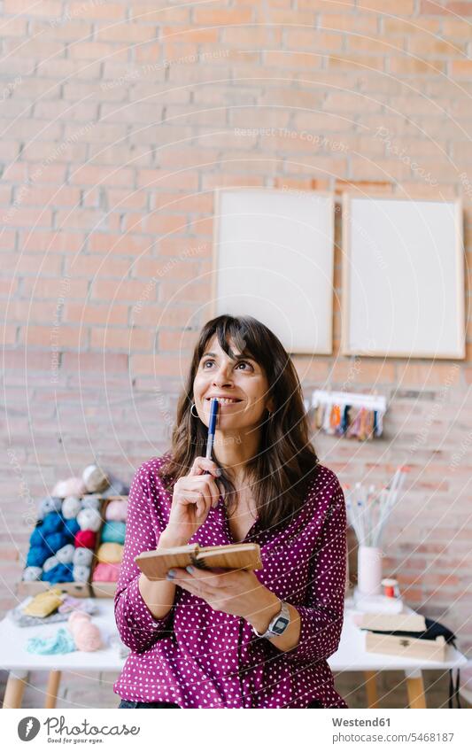 Lächelnde Frau im Strickstudio denkt nach und macht sich Notizen lächeln notieren weiblich Frauen Studio Atelier Studios Ateliers Strickzeug Erwachsener