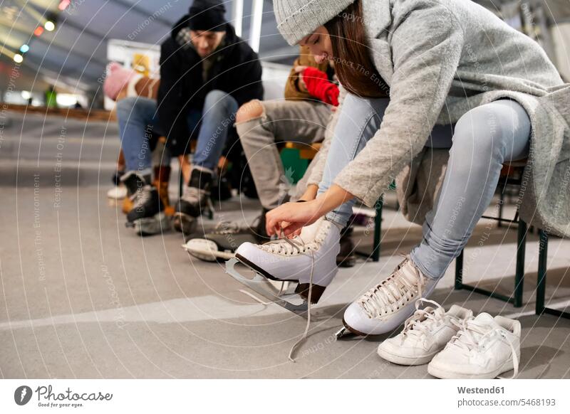 Freunde beim Anziehen von Schlittschuhen in einer Eishalle Eisbahn Eislaufbahn Schlittschuhbahn anziehen anlegen Freundschaft Kameradschaft Schlittschuhlaufen