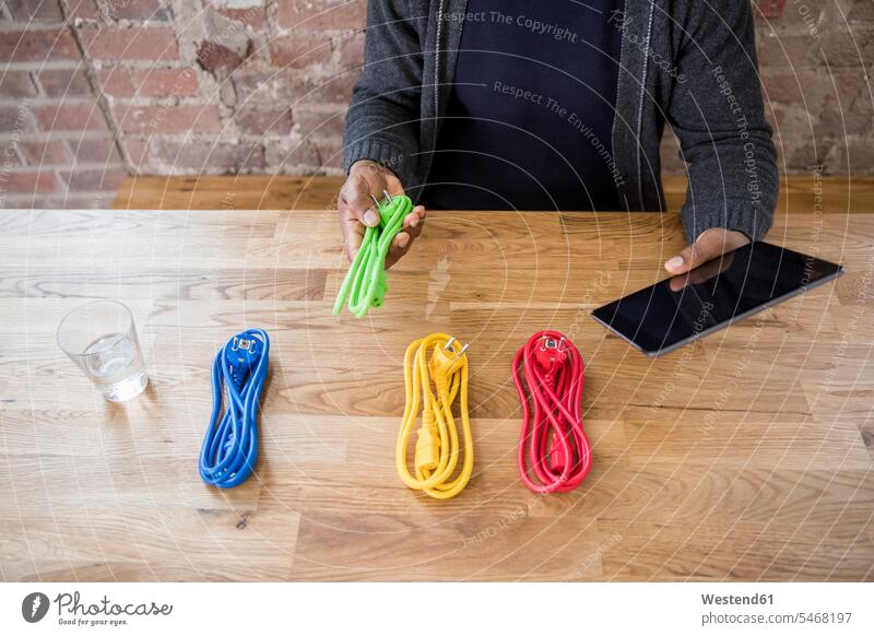 Geschäftsmann mit Tablettauswahl aus farbigen Stromkabeln auf der Tischplatte, Teilansicht Kabel Businessmann Businessmänner Geschäftsmänner Farbe Farbtöne