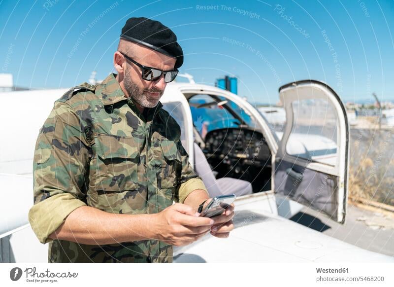 Textnachrichten für Armeesoldaten auf Smartphones während eines sonnigen Tages Farbaufnahme Farbe Farbfoto Farbphoto Außenaufnahme außen draußen im Freien