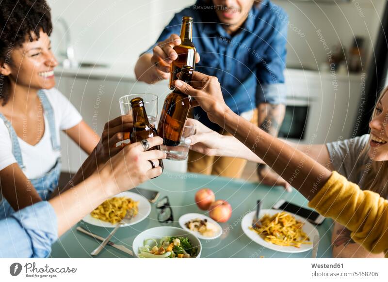 Fröhliche Freunde stoßen am Esstisch mit Bierflaschen an anstoßen zuprosten anstossen fröhlich Fröhlichkeit Frohsinn Heiterkeit Esstische Tisch Tische Alkohol