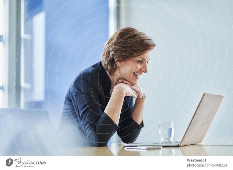 Glückliche Geschäftsfrau mit Laptop am Schreibtisch im Büro Job Berufe Berufstätigkeit Beschäftigung Jobs geschäftlich Geschäftsleben Geschäftswelt