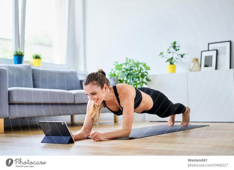 Lächelnde Frau lernt Plankenübung im Internet zu Hause Farbaufnahme Farbe Farbfoto Farbphoto Innenaufnahme Innenaufnahmen innen drinnen Innenausstattung