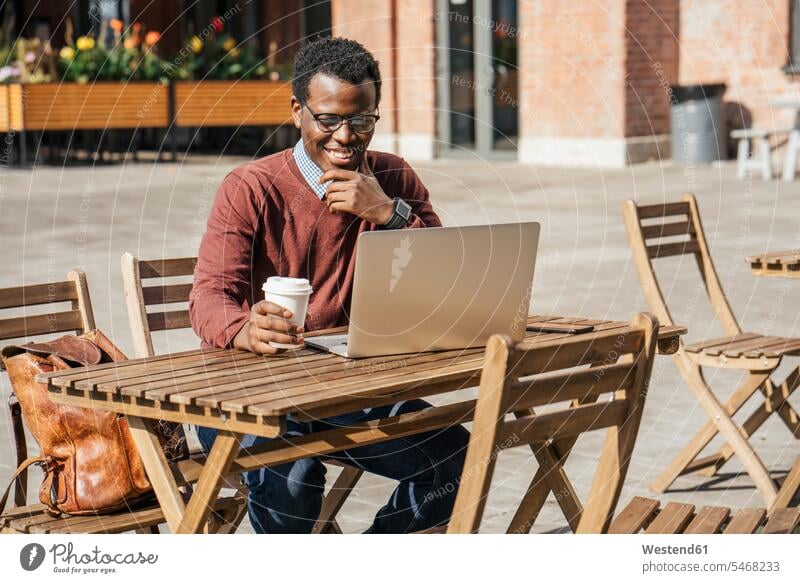 Junger Mann benutzt Laptop in einem Café und trinkt Kaffee Rechner Laptops Notebook Notebooks Brillen sitzend sitzt Glück glücklich sein glücklichsein zufrieden