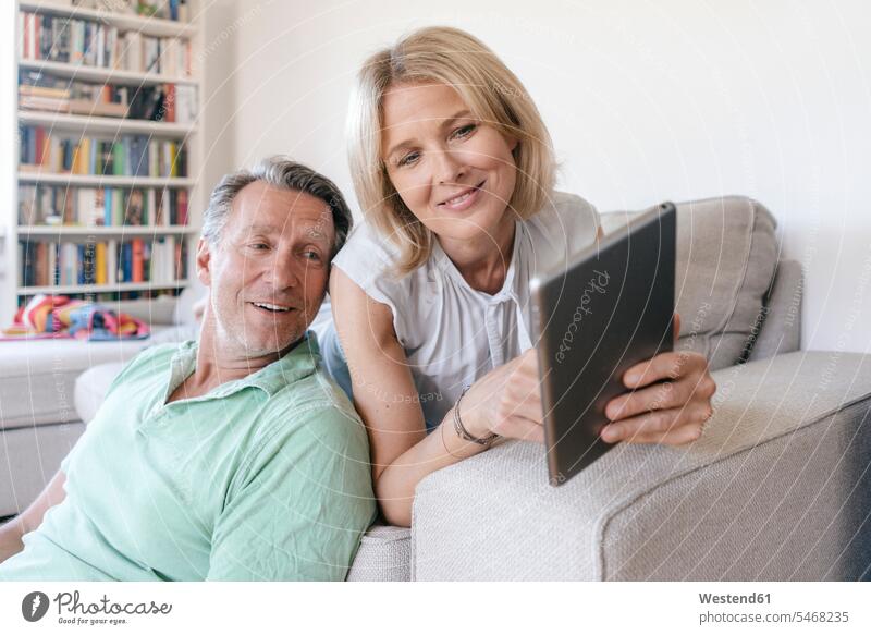 Lächelndes reifes Paar zu Hause mit Tablette Pärchen Paare Partnerschaft lächeln Zuhause daheim Tablet Computer Tablet-PC Tablet PC iPad Tablet-Computer Mensch