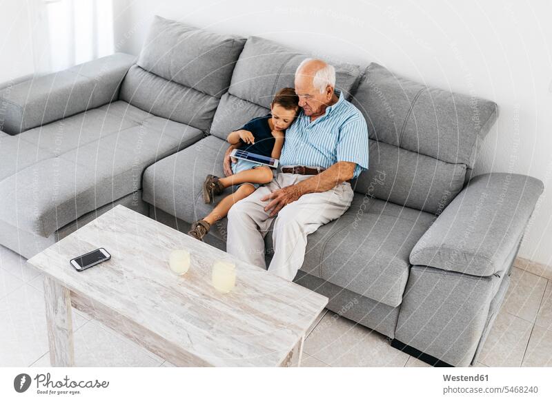 Großvater und Enkel sitzen zusammen auf der Couch zu Hause und schauen auf ein digitales Tablet Opa Großpapa Großpapas Opas Opi Großväter Opis Sofa Couches