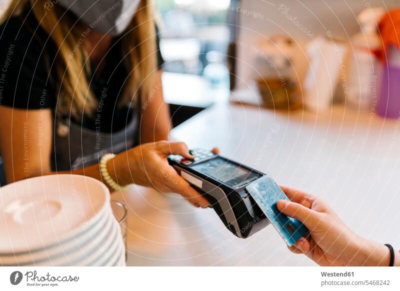 Weibliche Kassiererin, die während COVID-19 im Cafe eine Zahlung per Kreditkarte von einem Kunden erhält Farbaufnahme Farbe Farbfoto Farbphoto Tag