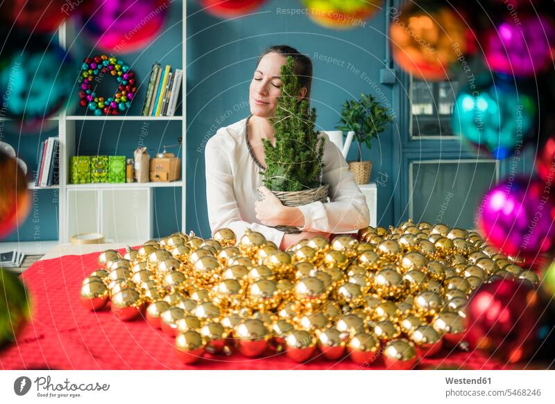 Frau sitzt am Tisch mit vielen goldenen Weihnachtskugeln, die eine Tanne halten weiblich Frauen Tannenbaum Tannenbäume goldfarben goldfarbene Christbaumkugel
