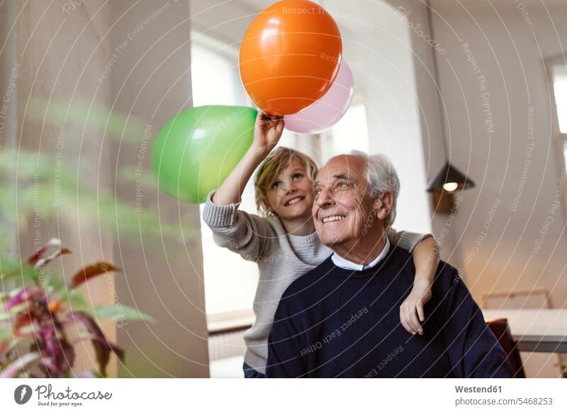 Glücklicher Großvater und Enkel, die zu Hause mit Luftballons spielen Generation Ballon Ballons Luftballone Arm umlegen Umarmung Umarmungen freuen Frohsinn