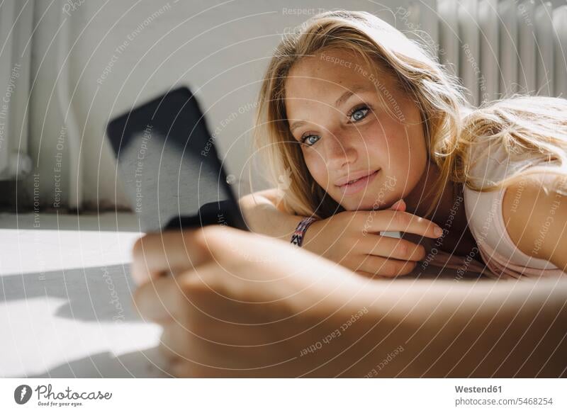 Blonde junge Frau liegt auf dem Boden und benutzt ihr Handy Heizluefter Heizlüfter Radiator Radiatoren Telekommunikation telefonieren Handies Handys