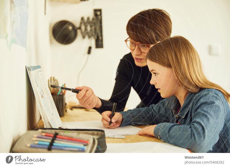 Mutter hilft Tochter bei den Hausaufgaben zu Hause Tische Arbeitstisch Schreibtische Stifte aufschreiben notieren schreibend Schrift sitzend sitzt reden daheim