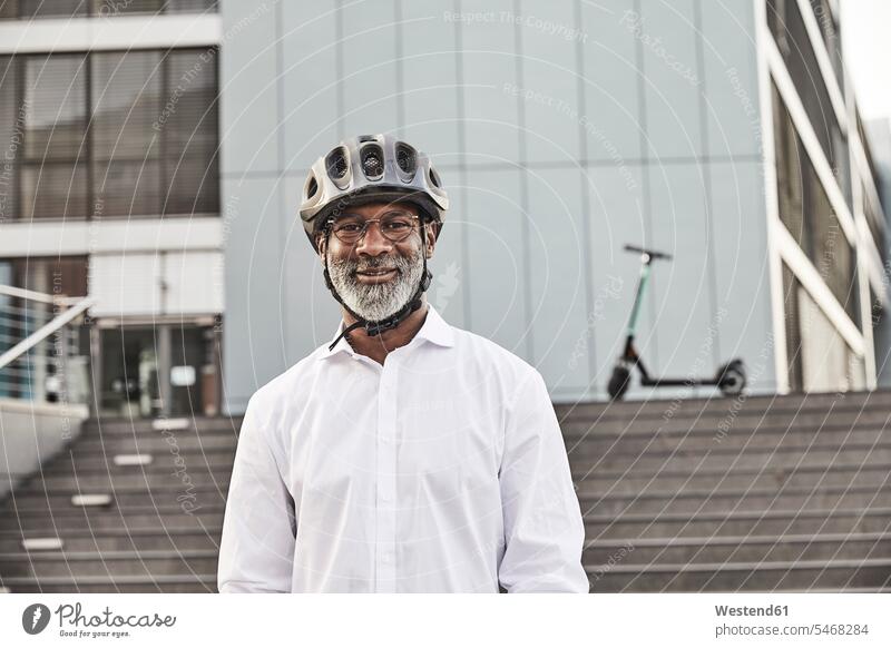 Porträt eines lächelnden reifen Geschäftsmannes mit E-Scooter und Fahrradhelm geschäftlich Geschäftsleben Geschäftswelt Geschäftsperson Geschäftspersonen