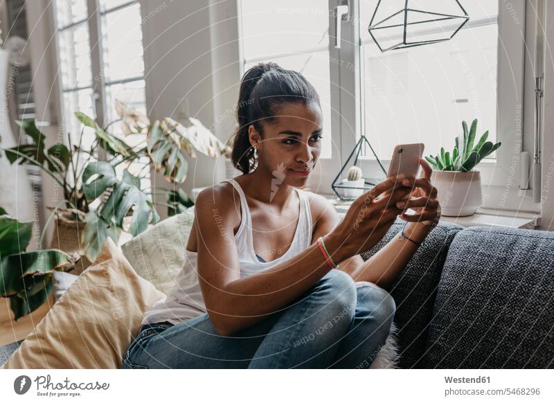 Porträt einer jungen Frau, die zu Hause auf der Couch sitzt und ein Selfie mit ihrem Mobiltelefon macht Selfies Smartphone iPhone Smartphones Portrait Porträts