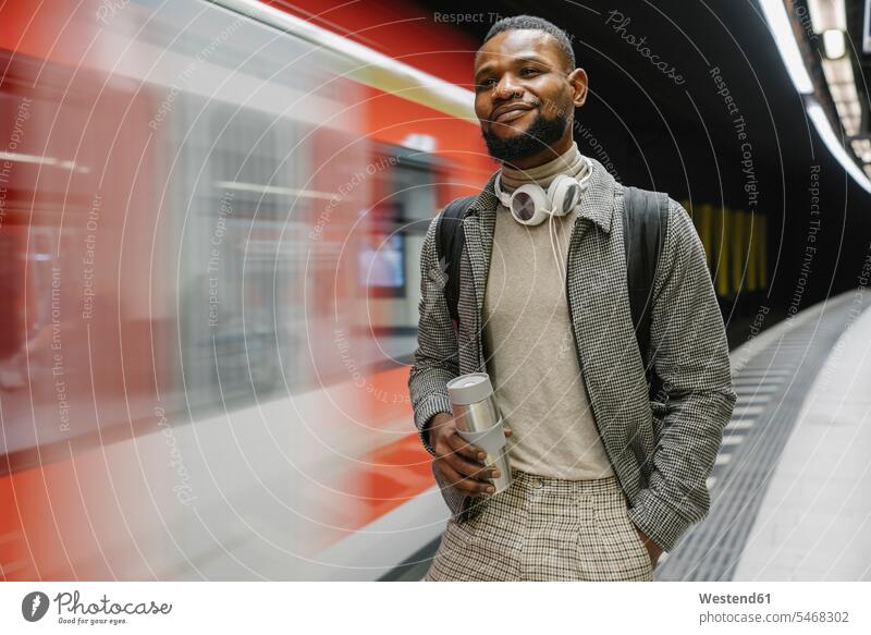 Stilvoller Mann mit wiederverwendbarer Tasse und Kopfhörern in einer U-Bahn-Station Touristen geschäftlich Geschäftsleben Geschäftswelt Geschäftsperson