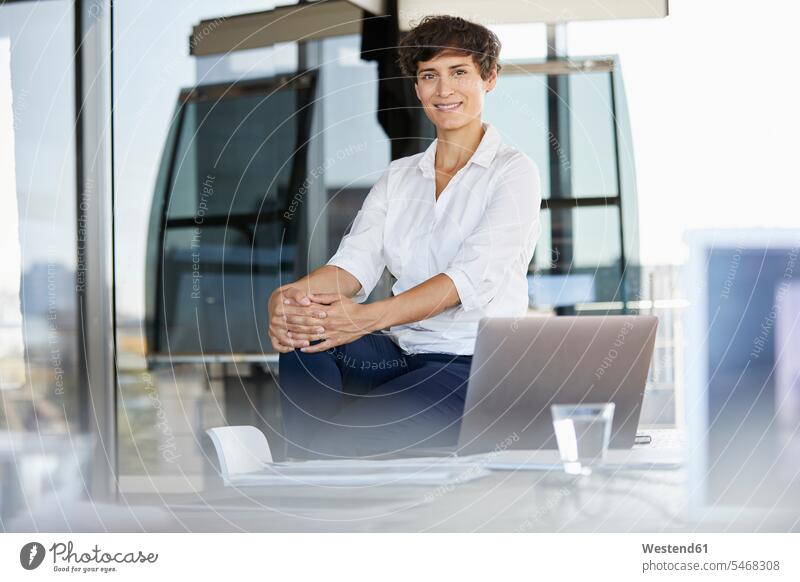 Porträt der selbstbewussten Geschäftsfrau sitzt auf dem Schreibtisch im Büro mit Laptop Notebook Laptops Notebooks Office Büros sitzen sitzend Portrait Porträts