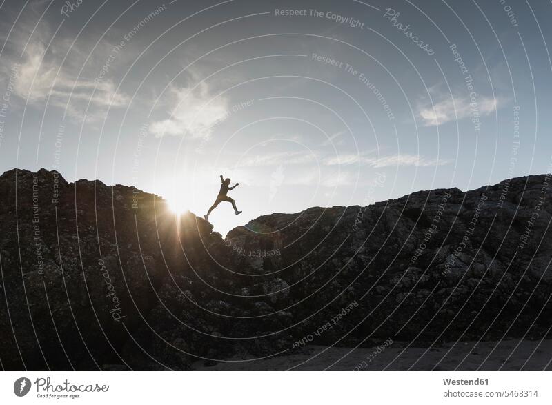 Frankreich, Bretagne, junger Mann springt bei Sonnenuntergang auf einen Felsen Männer männlich springen hüpfen Sonnenuntergänge Gestein Steine Erwachsener