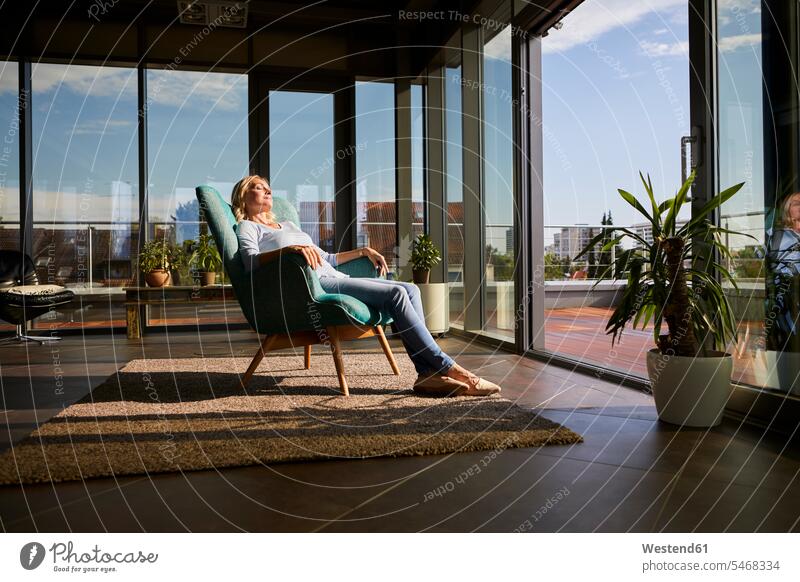 Reife Frau entspannt im Sessel im Sonnenlicht zu Hause weiblich Frauen Zuhause daheim entspanntheit relaxt Erwachsener erwachsen Mensch Menschen Leute People