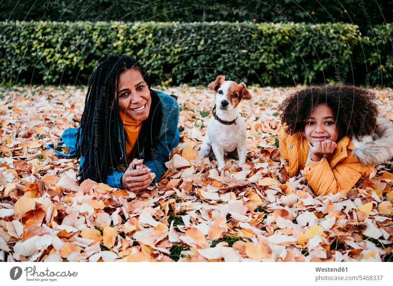 Lächelnde Frau und Tochter auf trockenem Blatt liegend mit Hund im Park sitzend Farbaufnahme Farbe Farbfoto Farbphoto Außenaufnahme außen draußen im Freien Tag