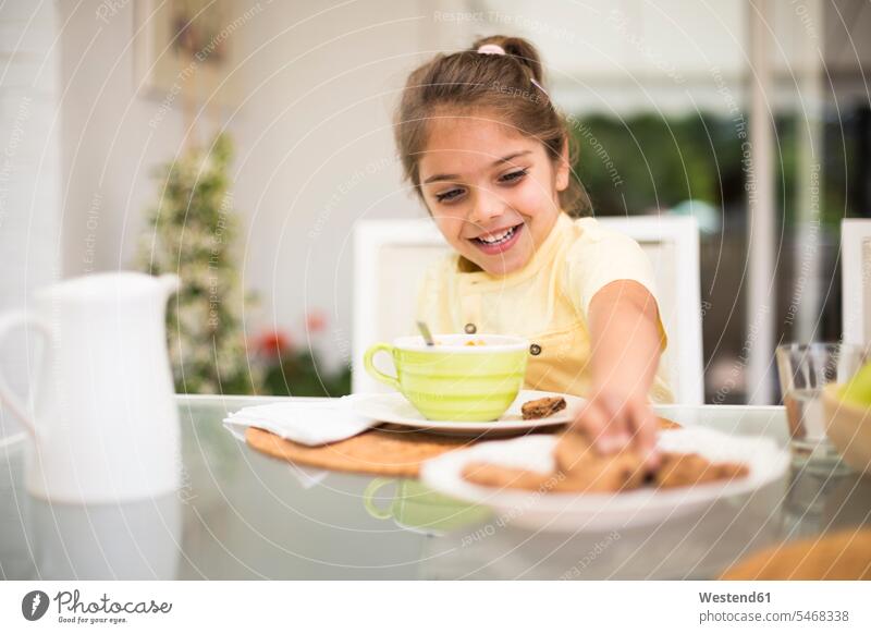 Glückliches kleines Mädchen nimmt einen Keks während des Frühstücks zu Hause nehmen aufnehmen Zuhause daheim Kekse Plaetzchen Plätzchen weiblich frühstücken