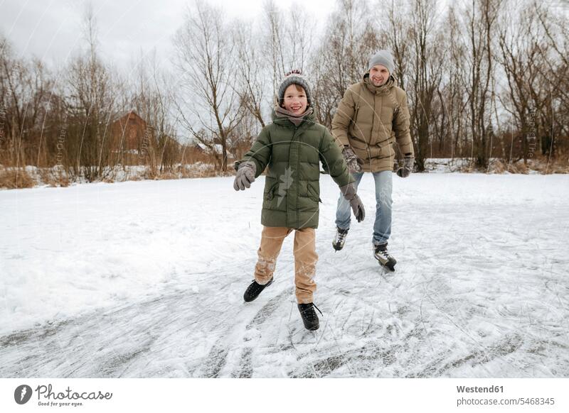 Glücklicher Junge läuft zusammen mit Vater auf dem Eis schneebedeckt Jahreszeiten winterlich Winterzeit warme Kleidung Winterkleidung Muße außen draußen