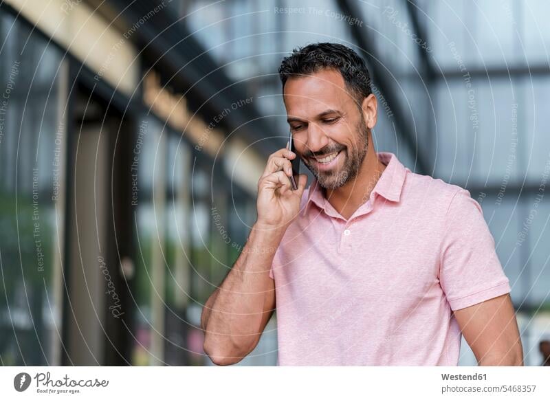 Lächelnder Mann am Mobiltelefon in der Stadt Freude freuen telefonieren anrufen Anruf telephonieren Unterhaltung Gespraech Gespräch Gespraeche Gespräche