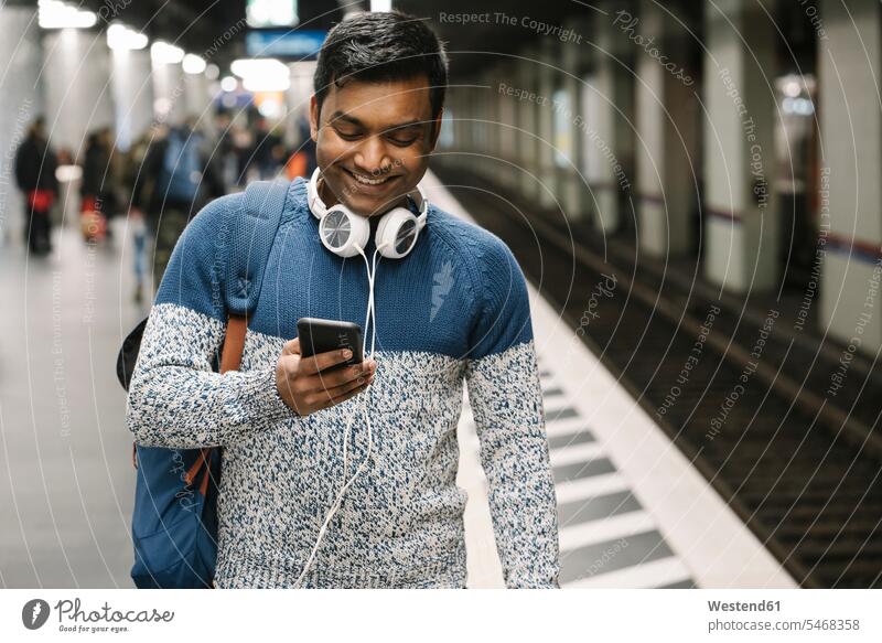 Lächelnder Mann benutzt Smartphone in U-Bahn-Station Touristen Rucksäcke Informationen Transport Transportwesen Bahnen Subway U-Bahnen Ubahn Ubahnen Underground