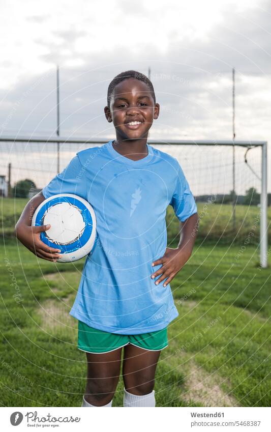 Porträt eines lächelnden jungen Fussballspielers, der den Ball auf dem Fussballplatz hält Junge Buben Knabe Jungen Knaben männlich Bälle Fußballspieler