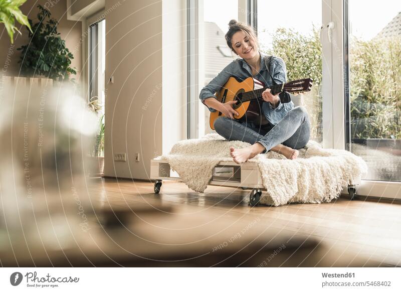 Lächelnde Frau sitzt am Fenster zu Hause Gitarre spielen Zuhause daheim weiblich Frauen Gitarren lächeln sitzen sitzend Erwachsener erwachsen Mensch Menschen