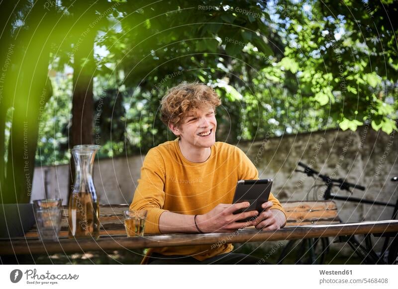 Porträt eines jungen Mannes am Biertisch im Garten sitzend mit digitalem Tablett Leute Menschen People Person Personen Europäisch Kaukasier kaukasisch 1 Ein