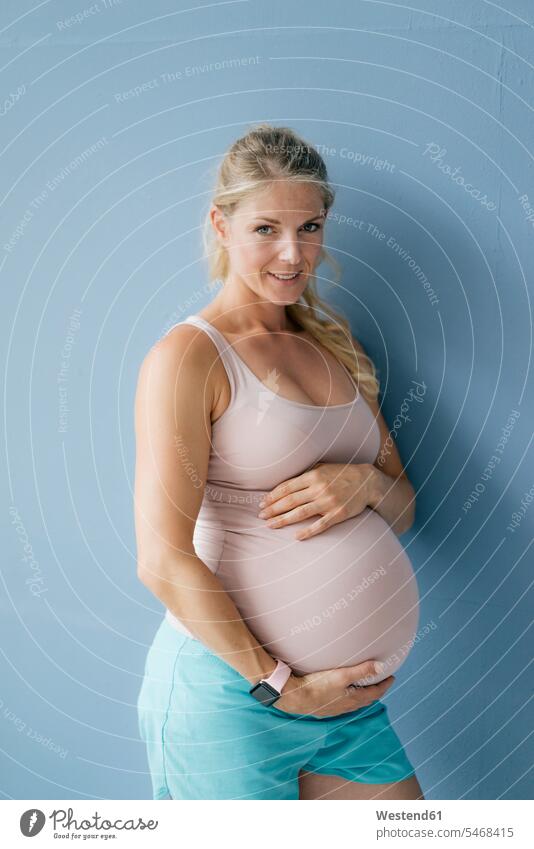 Porträt einer lächelnden schwangeren Frau, die an einer blauen Wand steht stehen stehend blauer blaues weiblich Frauen Portrait Porträts Portraits Schwangere