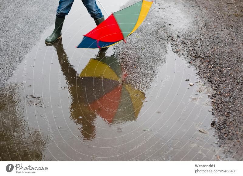 Kleiner Junge mit Regenschirm und Gummistiefeln steht in einer Pfütze, Teilansicht Pfützen Lache Buben Knabe Jungen Knaben männlich stehen stehend Regenschirme