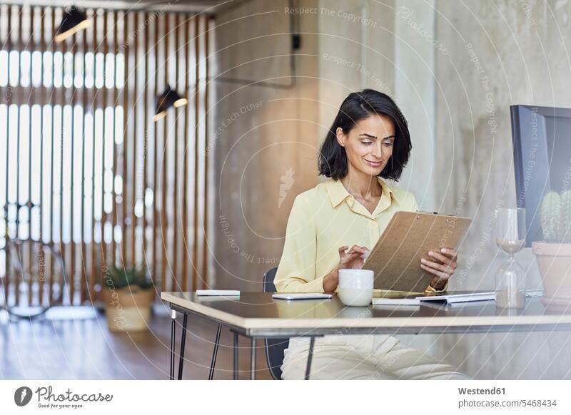 Geschäftsfrau hält Klemmbrett bei der Arbeit am Schreibtisch im Büro Farbaufnahme Farbe Farbfoto Farbphoto Deutschland Innenaufnahme Innenaufnahmen innen