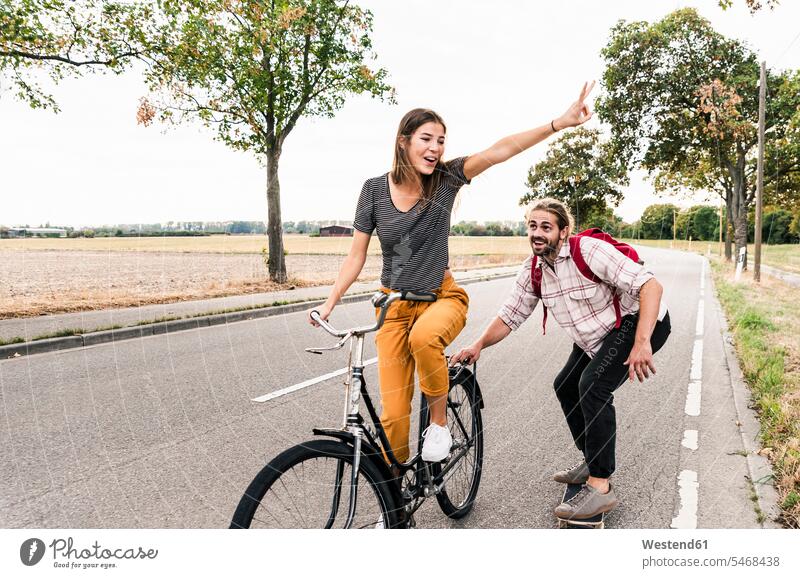 Glückliches junges Paar mit Fahrrad und Skateboard auf der Landstraße Bikes Fahrräder Räder Rad Landstraßen glücklich glücklich sein glücklichsein Pärchen Paare
