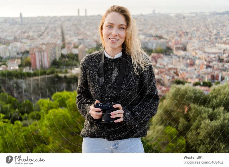 Porträt einer lächelnden jungen Frau mit Kamera bei Sonnenaufgang über der Stadt, Barcelona, Spanien Leute Menschen People Person Personen Europäisch Kaukasier