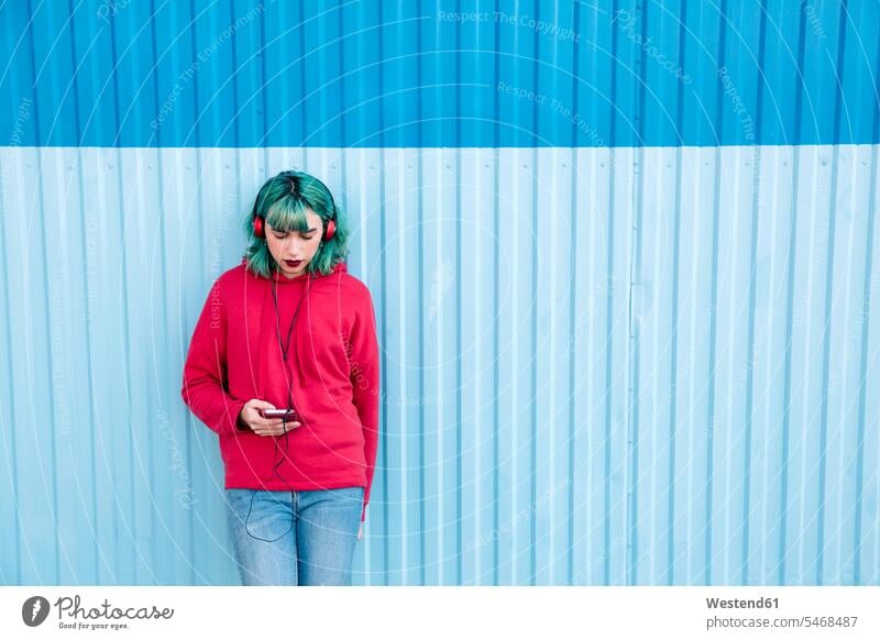 Junge Frau mit blau gefärbten Haaren hört Musik mit Kopfhörern beim Blick auf Smartphone blaue blauer blaues Portrait Porträts Portraits weiblich Frauen iPhone