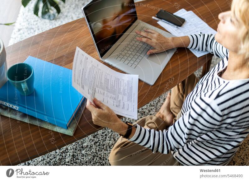 Reife Frau mit Dokumenten, die zu Hause einen Laptop benutzen Leute Menschen People Person Personen Alleinstehende Alleinstehender Singles Unverheiratete