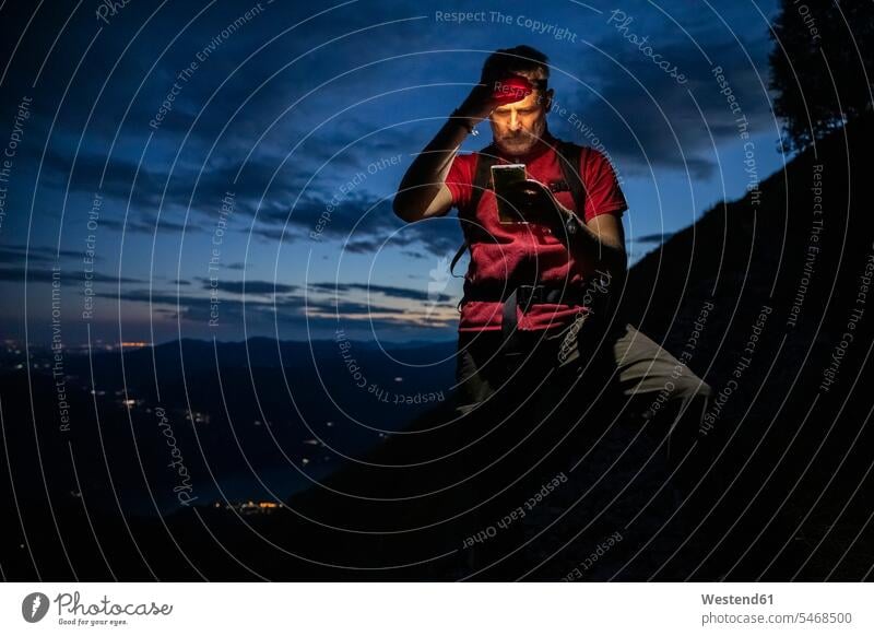 Männlicher Wanderer prüft Karte über Smartphone, während er nachts auf dem Berg steht, Orobie, Lecco, Italien Farbaufnahme Farbe Farbfoto Farbphoto Gebirge