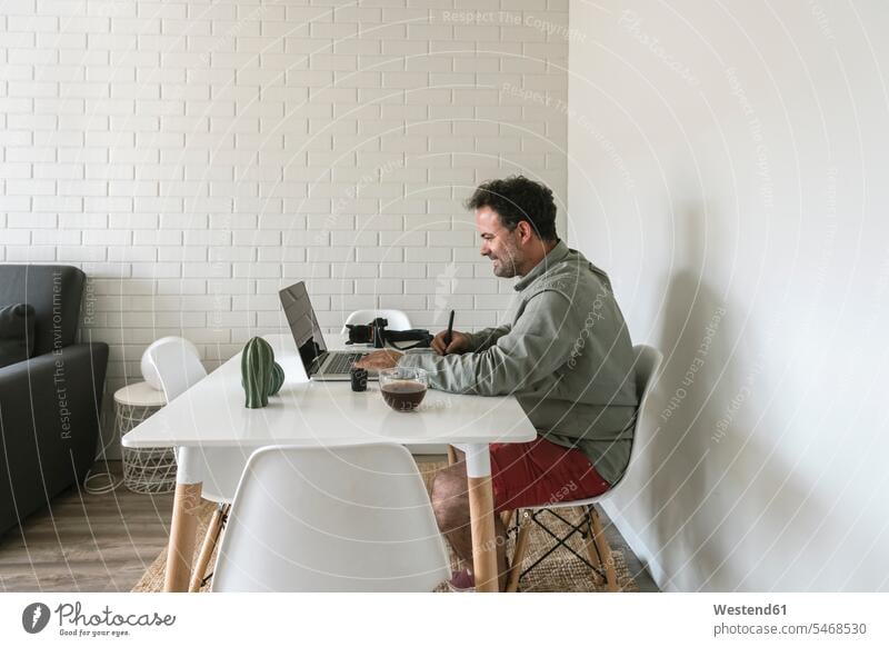 Mann sitzt am Tisch und arbeitet an Grafiktablett und Laptop Leute Menschen People Person Personen Europäisch Kaukasier kaukasisch 1 Ein ein Mensch eine