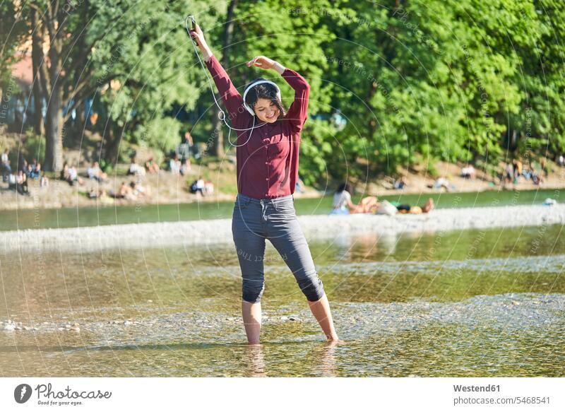 Glückliche junge Frau, die mit Kopfhörern und Handy Musik hört und am Flussufer tanzt tanzen tanzend Smartphone iPhone Smartphones weiblich Frauen Kopfhoerer