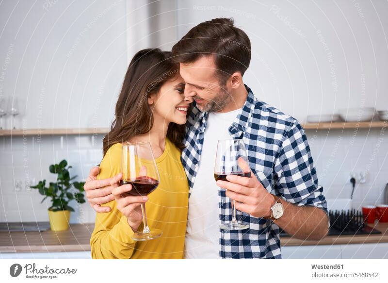 Glückliches Paar in der Küche stehend, mit den Armen um, trinken Rotwein, küssen Küsse Kuss Küchen steht liebevoll zaertlich einfühlsam einfuehlsam zärtlich