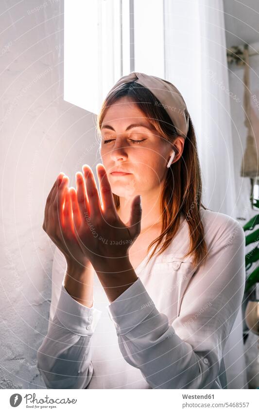 Schöne Frau betet zu Hause mit geschlossenen Augen am Fenster Farbaufnahme Farbe Farbfoto Farbphoto Spanien Innenaufnahme Innenaufnahmen innen drinnen Tag