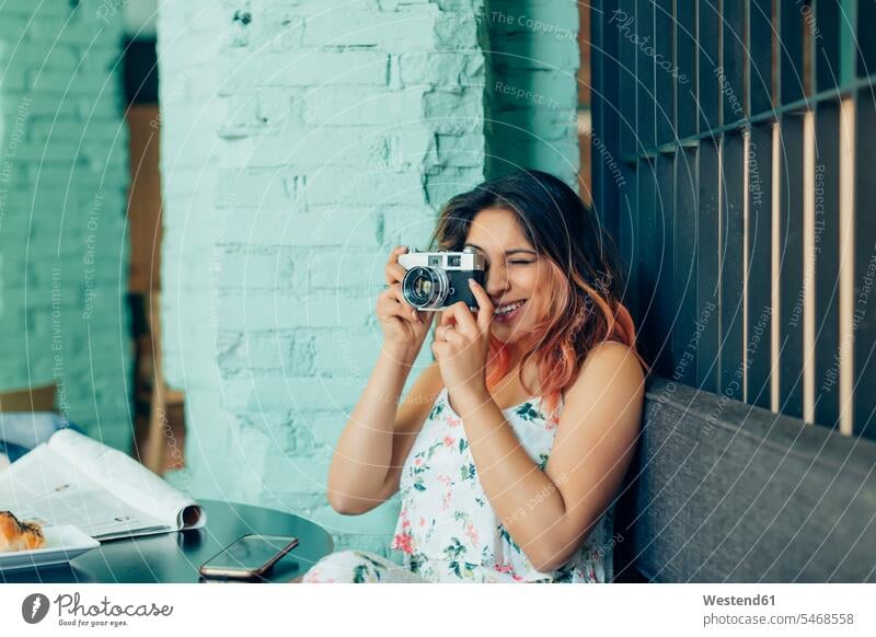 Lächelnde Frau sitzt im Café und macht Fotos mit der Kamera sitzen sitzend lächeln Cafe Kaffeehaus Bistro Cafes Kaffeehäuser Fotoapparat Fotokamera weiblich
