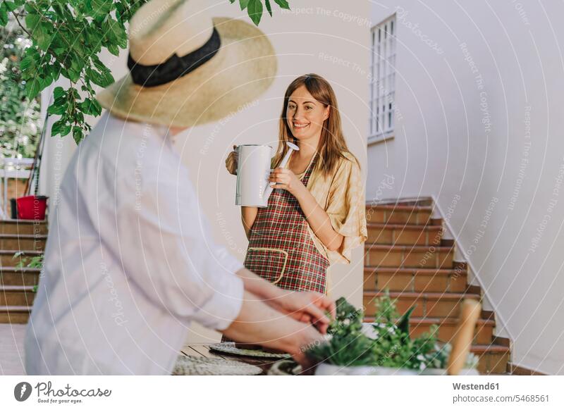 Ältere Frau mit Hut schaut auf Tochter, die eine Gießkanne gegen das Haus im Hof hält Farbaufnahme Farbe Farbfoto Farbphoto Spanien Freizeitbeschäftigung Muße