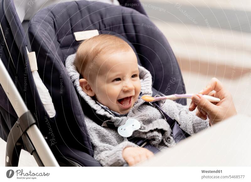 Mutter füttert lachendes Baby Junge im Kinderwagen Tisch Tische nicht erkennbare Person nicht erkennbare Personen unkenntliche Person unkenntliche Personen